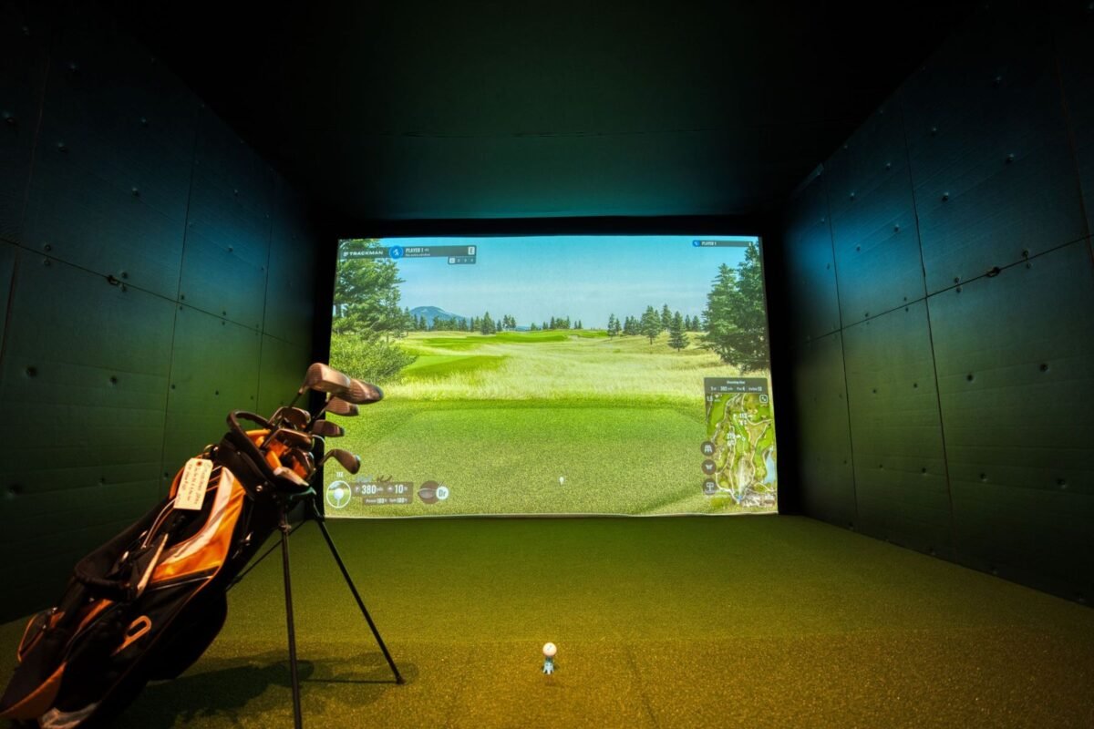 An indoor golf simulator bay with projection screen and hitting mat