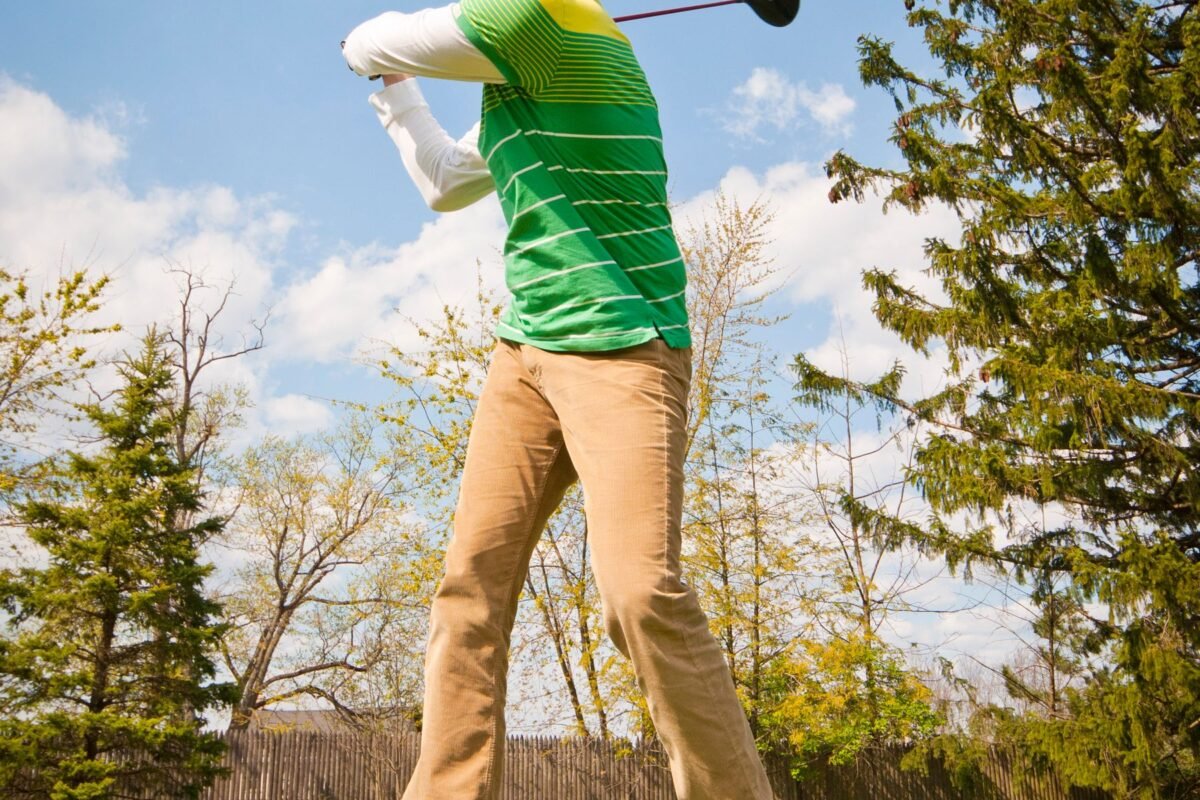 A golfer mid swing on the course, seen full length